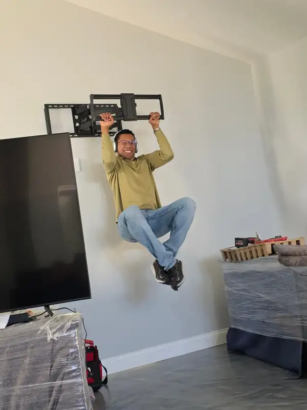 Tarick, owner of Tarick's TV Mounting, hanging from a full-motion TV mount secured to a wall in Melbourne, FL, before mounting a 75-inch TV