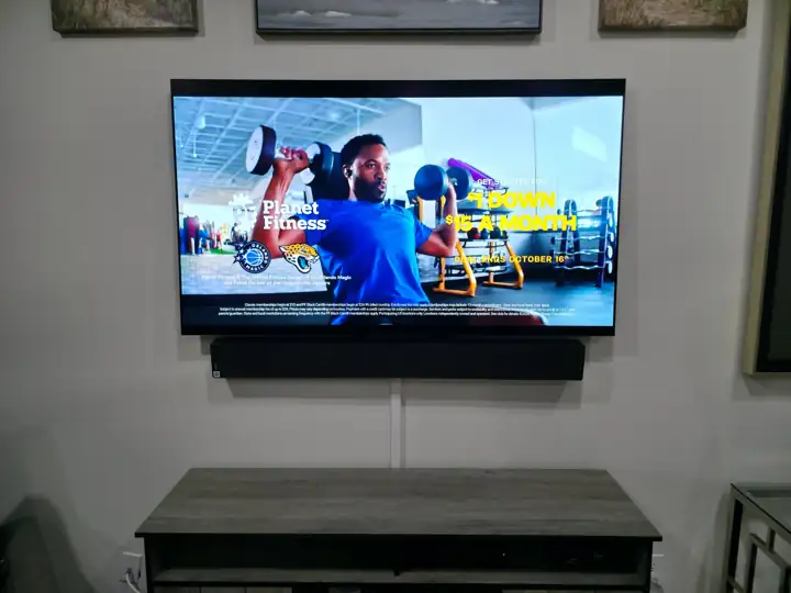 Large TV mounted above a TV stand in Melbourne, FL, with a soundbar mounted below it and the cords hidden in a white cord cover