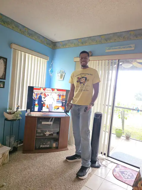 Tarick, owner of Tarick's TV Mounting, holding the remotes next to a TV he set up in Merritt Island, FL