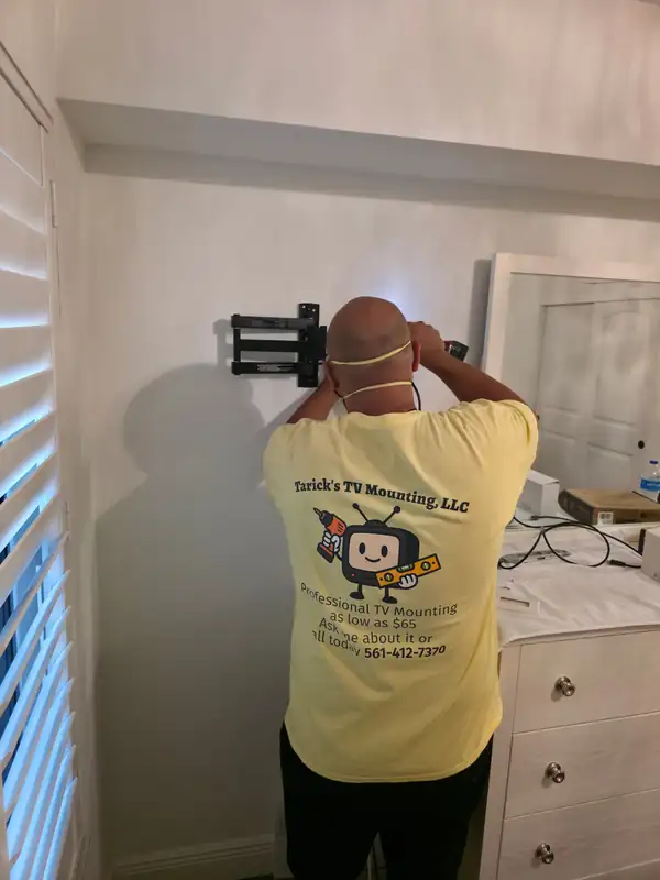 Noel, a Tarick's TV Mounting technician, installing in-wall wire management behind a full-motion TV mount in a Palm Beach Gardens, FL bedroom