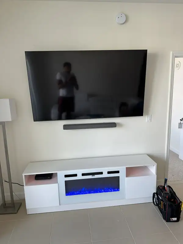 Large TV mounted above an electric fireplace TV console in a Palm Beach Gardens, FL living room, with a soundbar below it and no visible cables