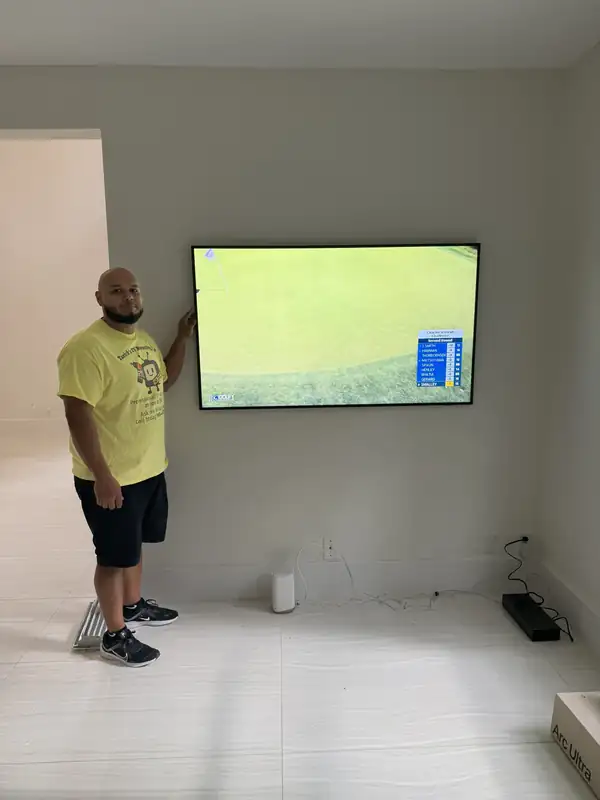 Noel, a Tarick's TV Mounting technician, next to a large TV he mounted on a living-room wall in Palm Beach Gardens, FL