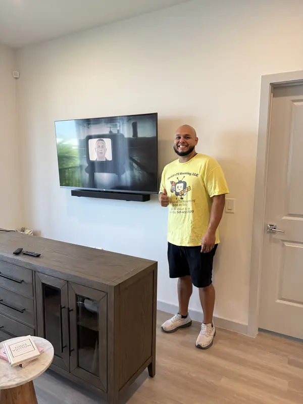 Noel, a Tarick's TV Mounting technician, next to a wall-mounted TV and soundbar he installed in Royal Palm Beach, FL